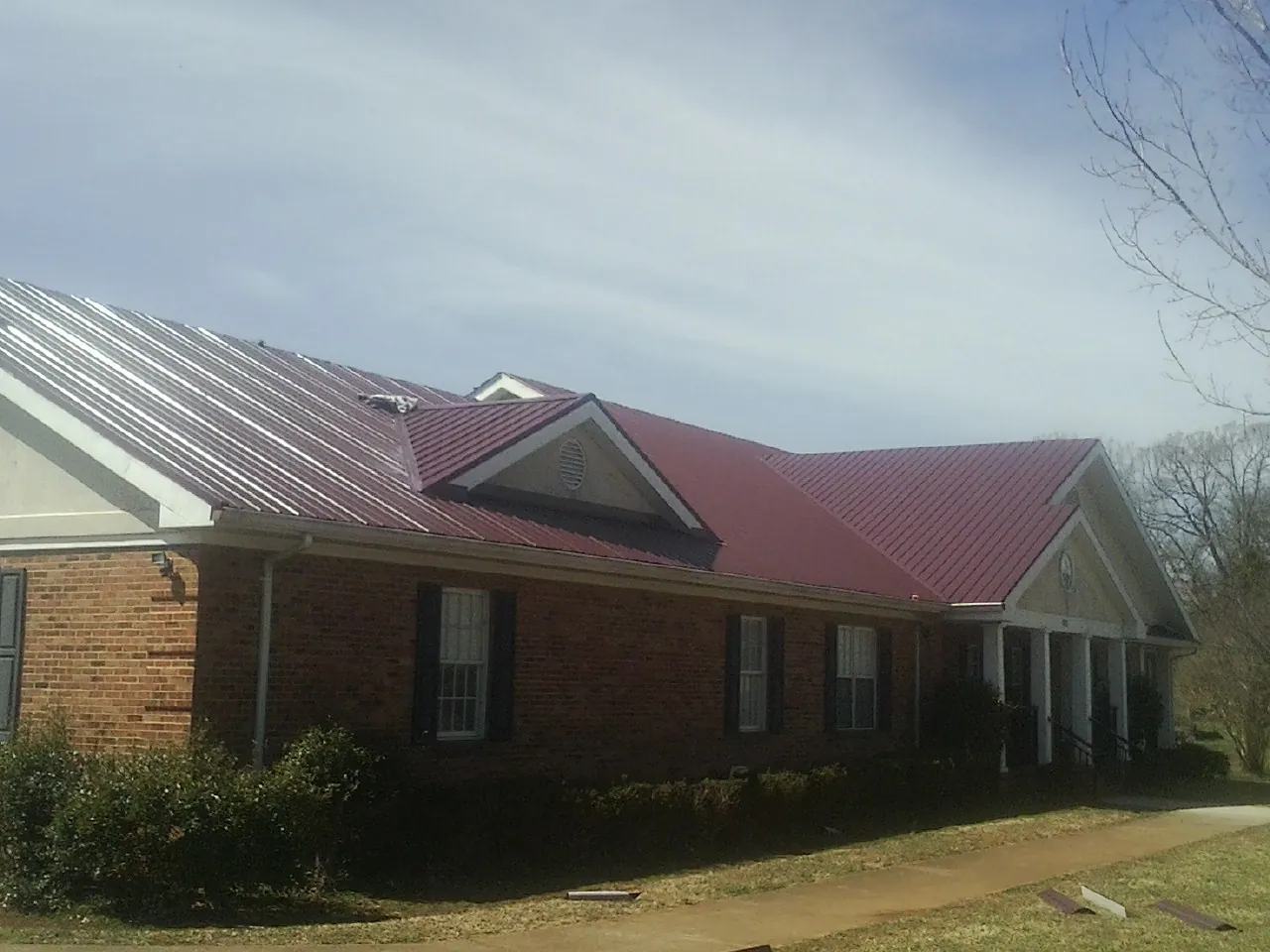 Red metal roof with gabled entries on a long brick building, from a Hail Damage Roof Repair job in Ray
