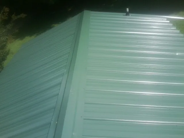 New green metal panels meeting at the ridge of a roof — Flat Roof Repair work by our crew in Ray