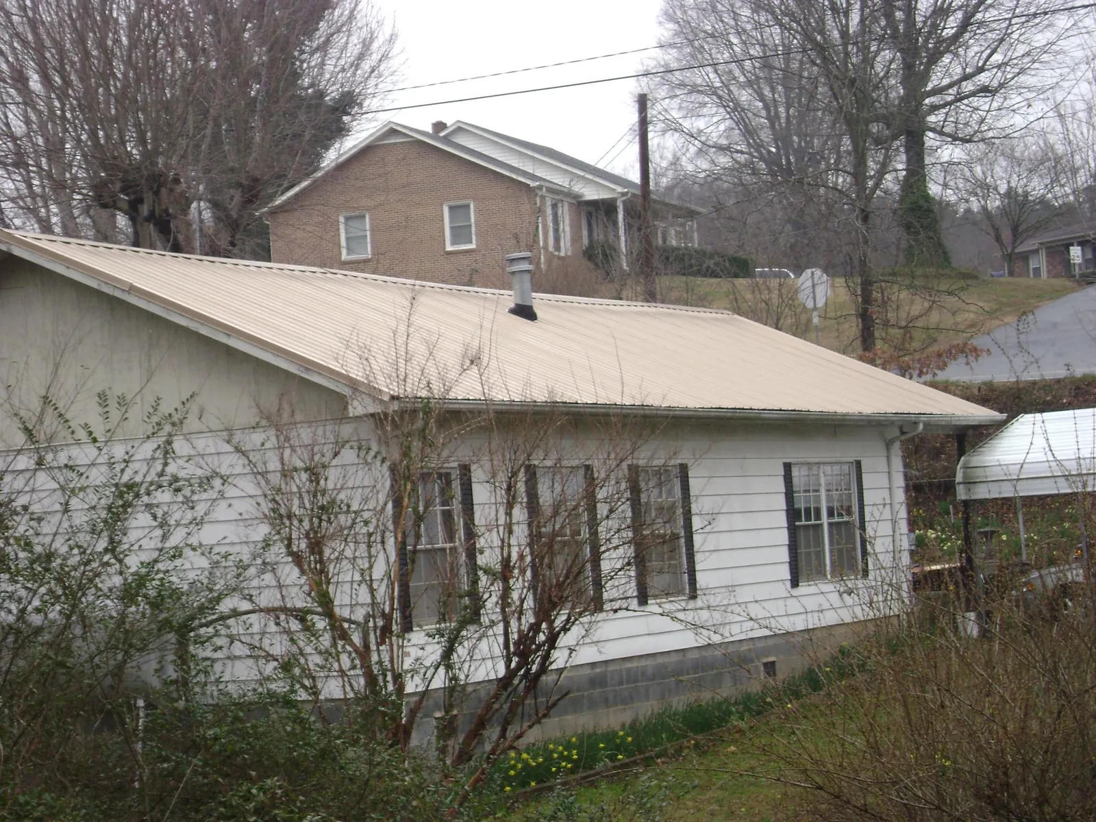 Tan metal roof on a white sided house set into a hillside — Commercial Roofing by Roofing Brothers in Ray