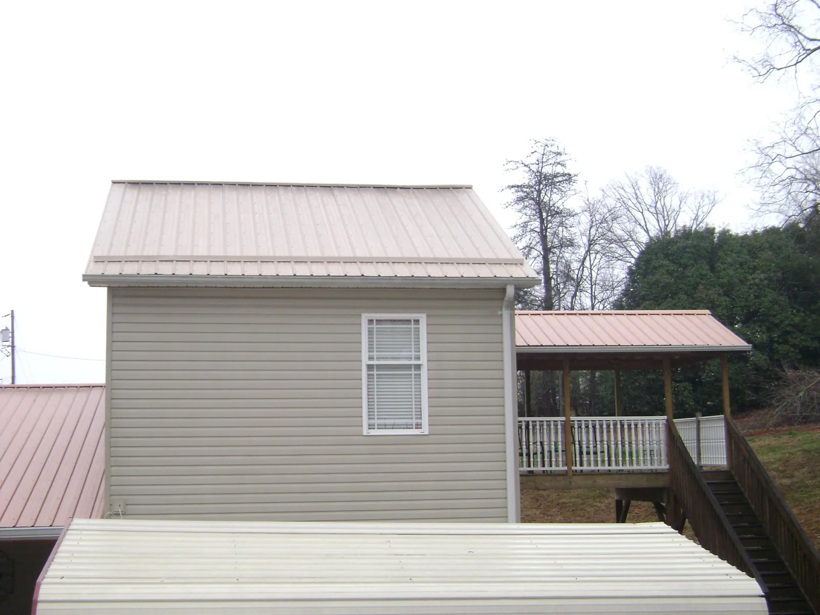 Tan metal roofs on a two story addition and attached porch, from a Roof Replacement job in Ray